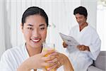 Woman in bathrobe having orange juice with boyfriend in background at home in the living room