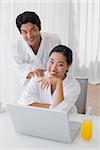 Couple in bathrobes using laptop together in the morning at home in the living room