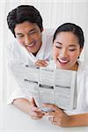 Couple in bathrobes reading newspaper together in the morning at home in the living room