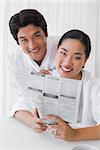 Couple in bathrobes reading newspaper together in the morning at home in the living room