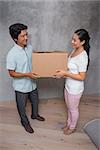 Happy couple holding a cardboard moving box in their new home