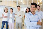 Casual boss smiling with arms crossed in front of business team in the office