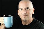 Close-up of a happy, peaceful bald man lifting his mug to camera.