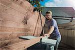 Joiner in backyard measuring planks of wood on workbench