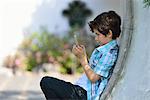 Boy leaning against curved wall texting on cellphone