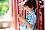 Boy leaning against red door texting on cellphone