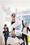 Three young businesswoman throwing papers mid air