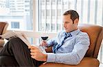Mid adult man relaxing at home with wine and newspaper