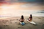 Two surfers, sitting on surfboards on beach, meditating