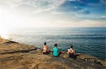 Women sitting on cliff top, looking at sea and meditating