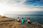 Women sitting on cliff top, looking at sea and meditating