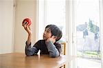 Boy sitting at table, holding an apple in front of him