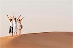 Children standing in desert with arms raised in air