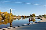 Australia, Australian Capital Territory (ACT), Canberra.  Man jogging beside Lake Burley Griffin with the National Carillon (belltower) in background.