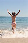 Happy woman raising arms and jumping in the sea