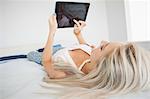 Gorgeous casual blonde using tablet in bright bedroom