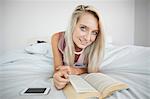 Gorgeous gleeful blonde reading a book in bright bedroom