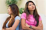 Two annoyed sisters sitting on a couch in the living room