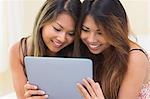 Two pretty sisters using a tablet while sitting on a couch in the living room