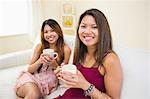 Two pretty sisters sitting in the living room on a couch and looking at the camera