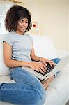 Pretty smiling brunette typing on her laptop in bright living room