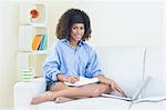 Pretty smiling student taking notes using laptop in bright living room