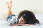 Pretty smiling brunette lying on bed resting head on hand in bright bedroom