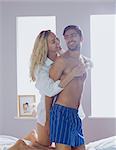 Blonde woman embracing her boyfriend while kneeling on the bed