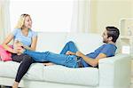 Happy blonde woman massaging the feet of her boyfriend sitting in the living room