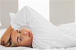 Peaceful blonde wearing white shirt lying on bed at home in bedroom