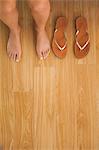 Woman sitting on edge of bed beside her sandals at home in bedroom