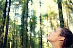 Fascinated young woman sitting in the middle of a forest looking upwards