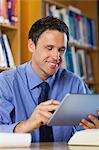 Cheerful librarian sitting at desk using tablet in library in a college