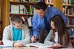 Lecturer explaining something to students and pointing at book in library in a college