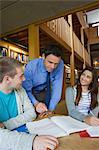 Handsome lecturer explaining something to students in library in a college