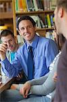 Smiling lecturer explaining something to group of students in library in a college