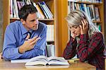 Lecturer explaining something to frustrated blonde student in library in a college