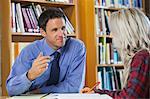 Smiling lecturer explaining something to blonde student in library in a college