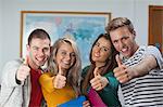 Cheerful casual students showing thumbs up in hallway in a college