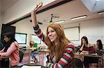 Smiling female student raising her hand in class at the university