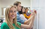 Students writing on the whiteboard together in class with one smiling at camera at the university