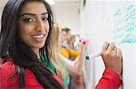 Student writing on the whiteboard in class smiling at camera at the university