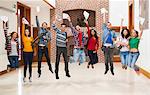 Happy students jumping for joy holding exam results in a hallway at the university