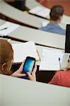 Student sitting in a lecture hall using her smartphone in college