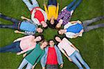 Group of students smiling at camera lying in circle on the grass on campus at the university