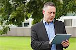 Serious lecturer using his tablet outside on campus at the university