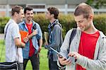 Cheerful male student using his tablet in front of his classmates outside at the university