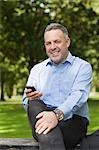 Smiling professor texting on phone while sitting on bench on campus at the university