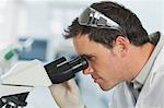 Handsome young scientist looking through a microscope in a laboratory