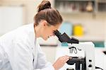 Smiling brunette student looking through microscope in lab at college